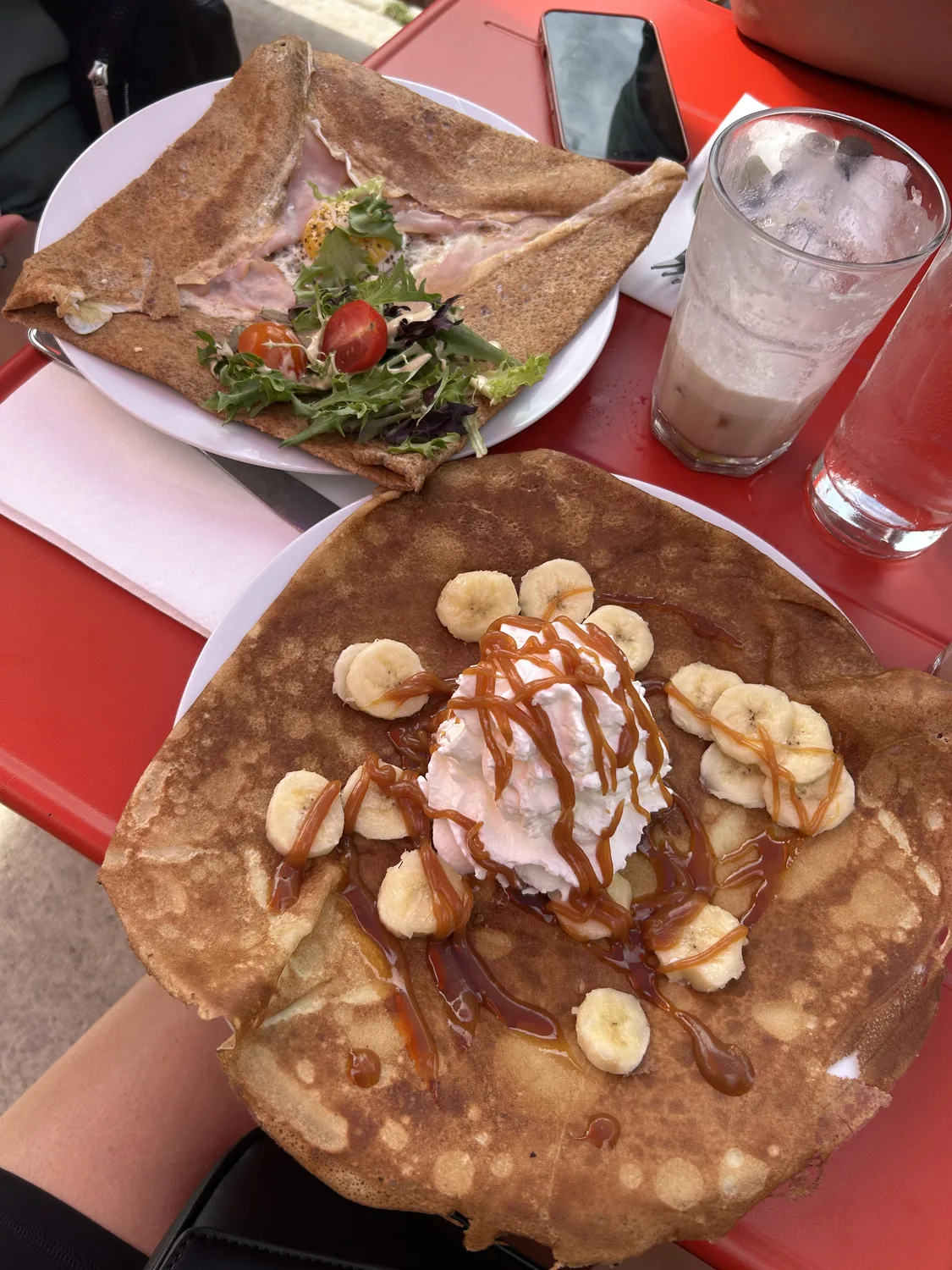 A savoury buckwheat galette with ham and egg beside a banana-caramel sweet crêpe on the patio at Paris Crêpes Café